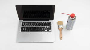 Geoeffneter Laptop auf weisser Flaeche mit Pinsel und Druckluftspray